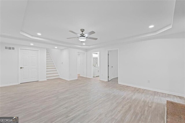 unfurnished living room featuring a raised ceiling, stairway, recessed lighting, a ceiling fan, and light wood-style floors