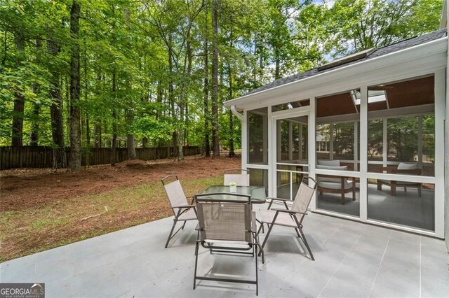 view of patio with a sunroom, fence, and outdoor dining area
