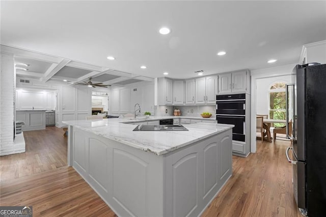 kitchen featuring black appliances, light wood-style flooring, ceiling fan, light stone counters, and coffered ceiling