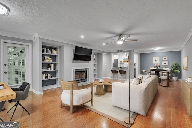 1015 Dunbar Dr, Dunwoody, GA 30338 - unfurnished living room featuring a ceiling fan, built in features, a textured ceiling, crown molding, and light wood-style floors