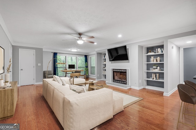 1015 Dunbar Dr, Dunwoody, GA 30338 - living area featuring ornamental molding, light wood-style flooring, a fireplace with raised hearth, built in shelves, and a ceiling fan
