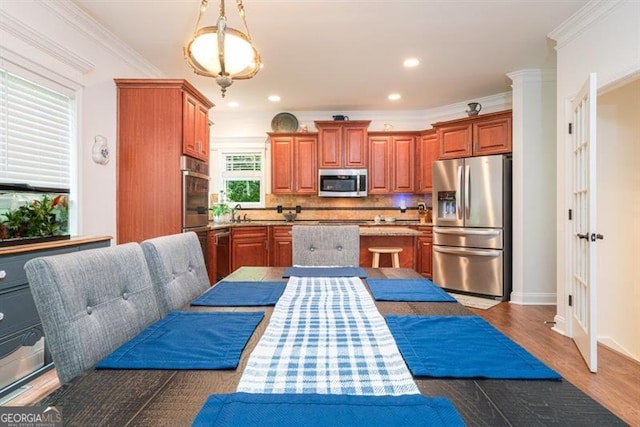 kitchen with stainless steel appliances, backsplash, ornamental molding, dark wood-style floors, and brown cabinets