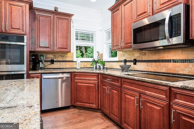 kitchen with stainless steel appliances, tasteful backsplash, light stone counters, light wood finished floors, and ornamental molding