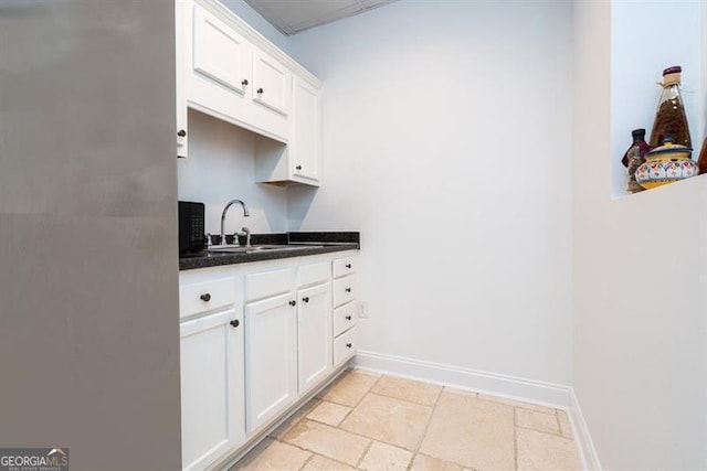 kitchen featuring a sink, white cabinetry, baseboards, and stone tile flooring