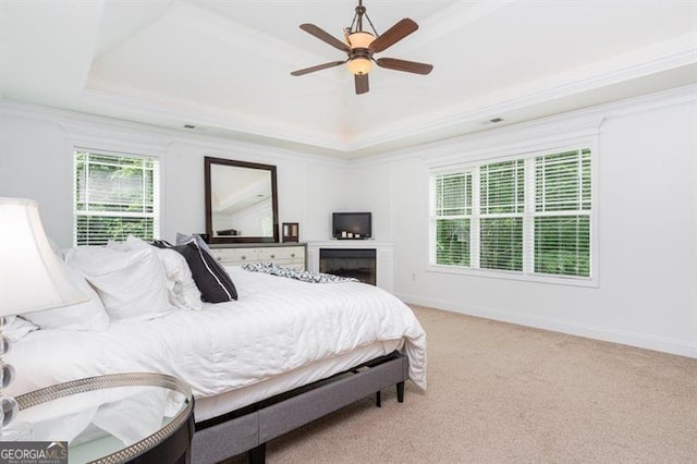 bedroom featuring a raised ceiling, light carpet, ornamental molding, a ceiling fan, and baseboards
