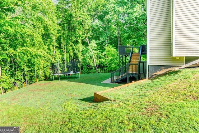 view of green lawn with a trampoline and stairway