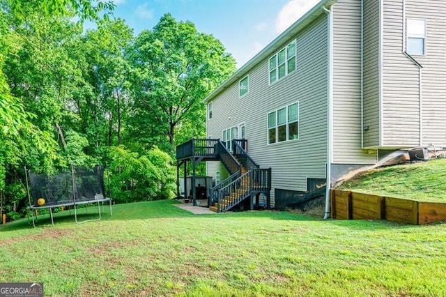 back of house with a trampoline, stairway, a wooden deck, and a lawn