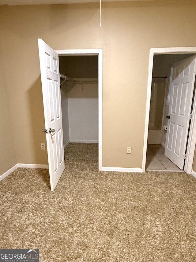 unfurnished bedroom with carpet flooring, a walk in closet, a closet, and baseboards