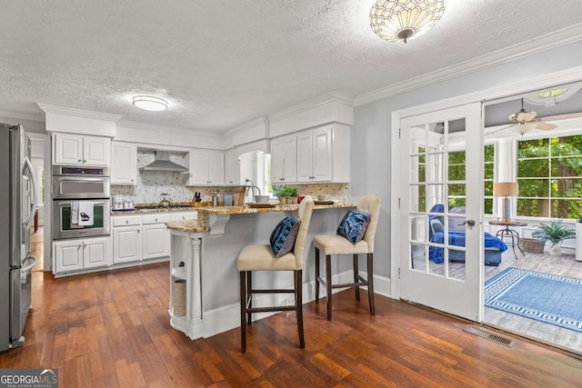 3441 Sherrod Dr SW, Marietta, GA 30060 - kitchen with wall chimney exhaust hood, stainless steel appliances, a peninsula, dark wood-style flooring, and a textured ceiling