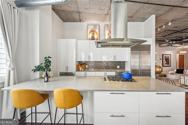 206 NE 11th St NE Unit Ph703, Atlanta, GA 30309 - kitchen featuring appliances with stainless steel finishes, island exhaust hood, white cabinetry, a sink, and decorative backsplash
