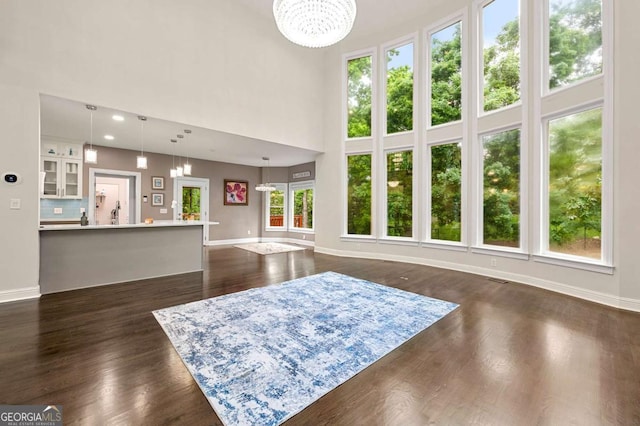 living room with a chandelier, a towering ceiling, baseboards, and dark wood-type flooring