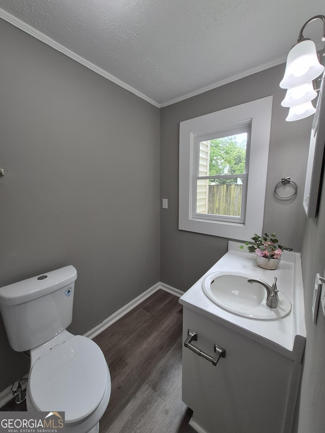 bathroom with wood finished floors, crown molding, toilet, baseboards, and vanity