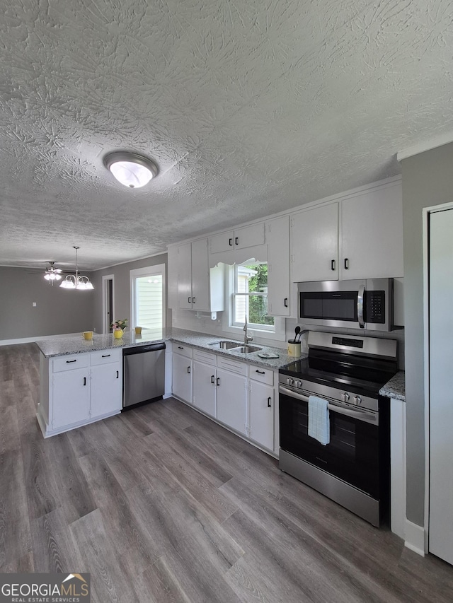 kitchen with stainless steel appliances, a peninsula, a sink, white cabinets, and a textured ceiling