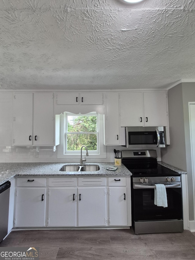 kitchen featuring appliances with stainless steel finishes, a sink, white cabinetry, wood finished floors, and a textured ceiling