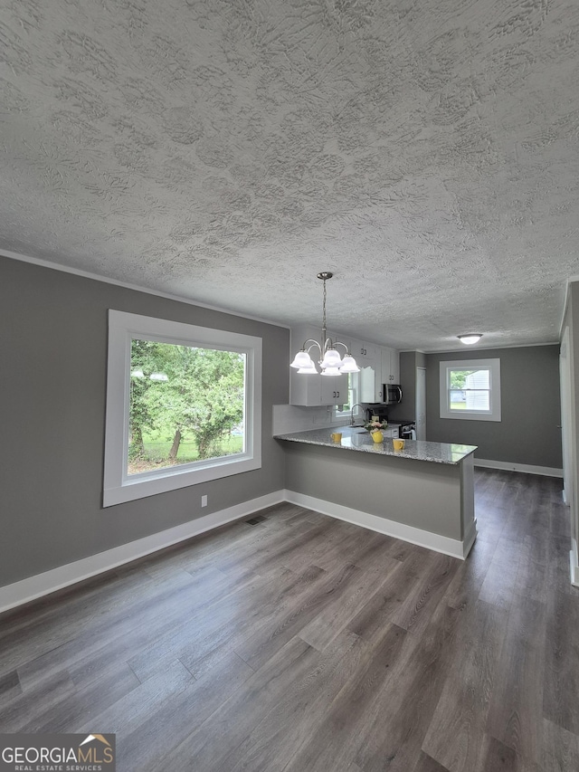 unfurnished dining area featuring a chandelier, dark wood finished floors, baseboards, a sink, and a textured ceiling