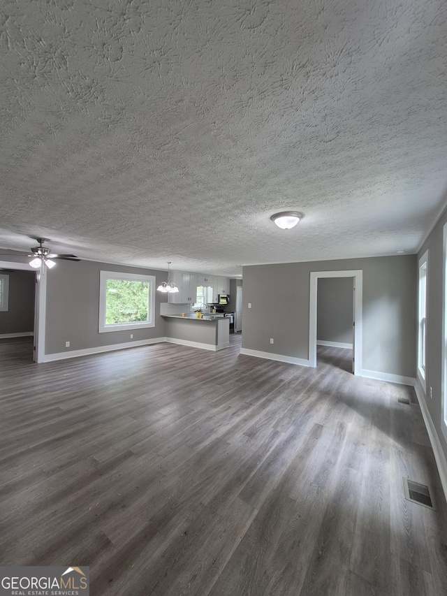unfurnished living room featuring baseboards, dark wood-style flooring, a chandelier, a ceiling fan, and a textured ceiling