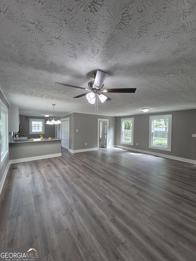 unfurnished living room with dark wood-type flooring, ceiling fan, a chandelier, baseboards, and a textured ceiling