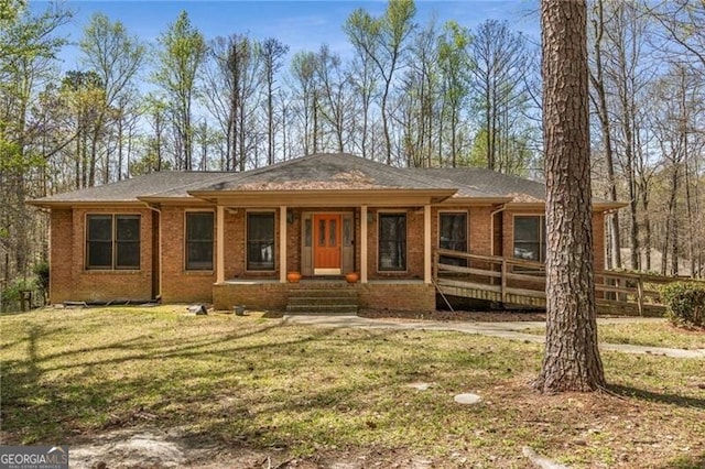 view of front of house featuring brick siding, a front lawn, covered porch, and a shingled roof