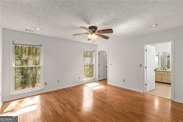 unfurnished bedroom featuring a textured ceiling, light wood finished floors, baseboards, recessed lighting, and ensuite bath