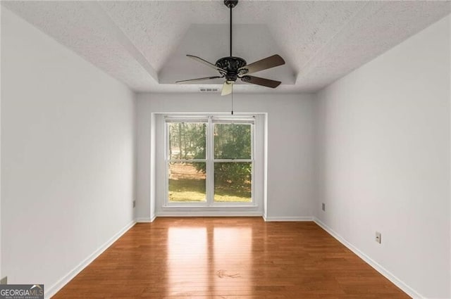 unfurnished room featuring a raised ceiling, a ceiling fan, wood finished floors, a textured ceiling, and baseboards