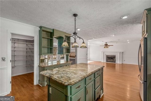 kitchen featuring green cabinets, a ceiling fan, freestanding refrigerator, a center island, and wood finished floors