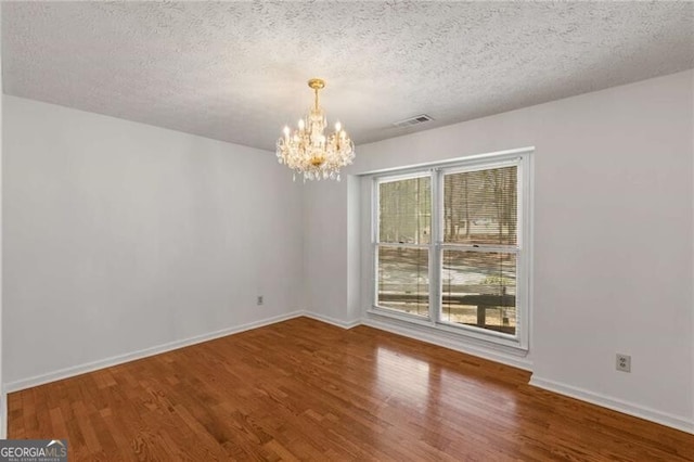 unfurnished dining area with a chandelier, wood finished floors, baseboards, and a textured ceiling
