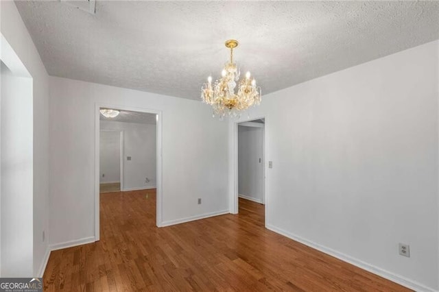 unfurnished dining area featuring a textured ceiling, a chandelier, wood finished floors, and baseboards