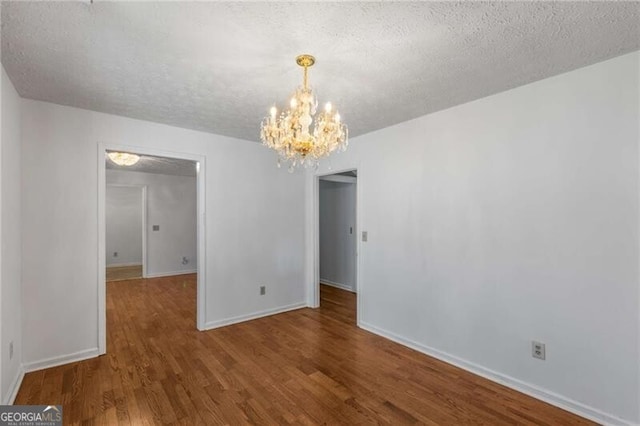 unfurnished dining area with a chandelier, wood finished floors, baseboards, and a textured ceiling