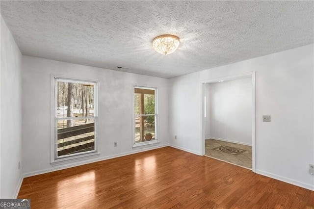 unfurnished room with wood finished floors, a textured ceiling, and baseboards