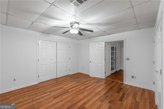 unfurnished bedroom featuring a paneled ceiling, wood finished floors, baseboards, and a ceiling fan