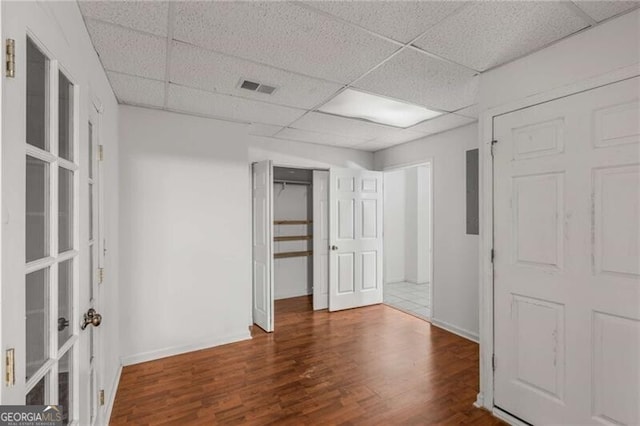 unfurnished bedroom with a drop ceiling, wood finished floors, and baseboards