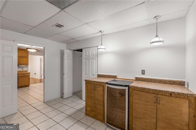 kitchen featuring brown cabinets, a paneled ceiling, light tile patterned floors, pendant lighting, and fridge
