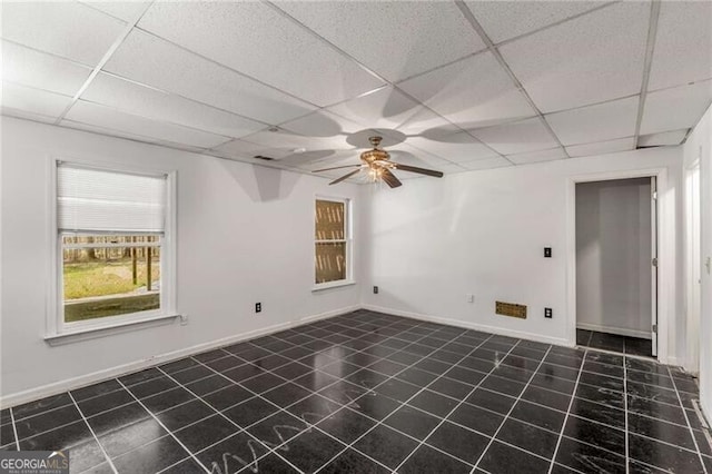 unfurnished room with a paneled ceiling, dark tile patterned flooring, a ceiling fan, and baseboards