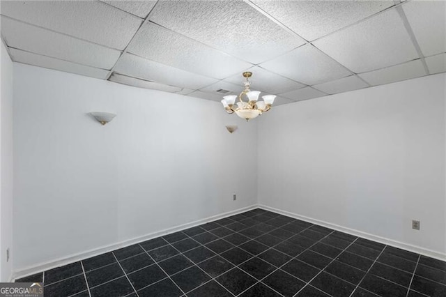 spare room featuring dark tile patterned flooring, a drop ceiling, a chandelier, and baseboards
