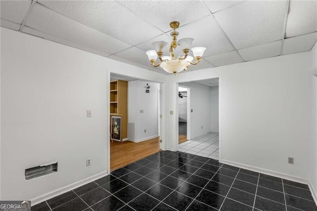 unfurnished dining area featuring a chandelier, a drop ceiling, tile patterned floors, and baseboards