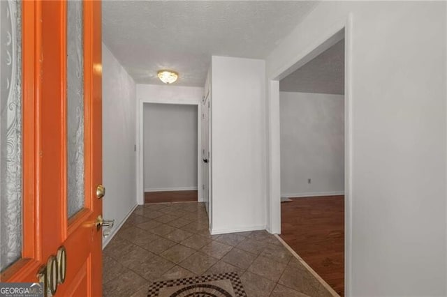 hallway featuring dark tile patterned floors, baseboards, and a textured ceiling