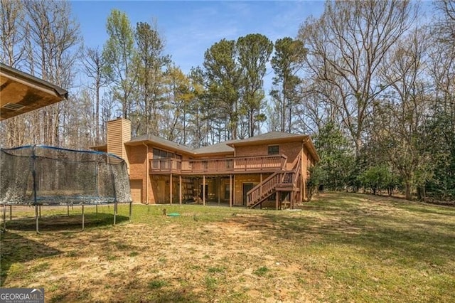 back of house with a trampoline, stairway, a deck, a lawn, and a chimney