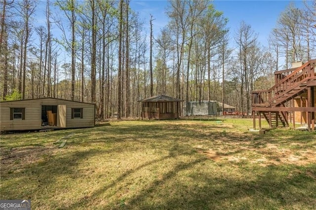view of green lawn with a trampoline, stairway, an outbuilding, and a deck
