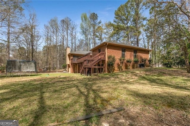 back of house featuring a trampoline, stairway, a deck, and a yard
