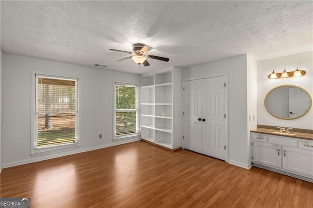 unfurnished bedroom featuring a sink, light wood finished floors, a textured ceiling, baseboards, and ensuite bathroom