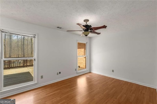 empty room featuring ceiling fan, a textured ceiling, plenty of natural light, wood finished floors, and baseboards