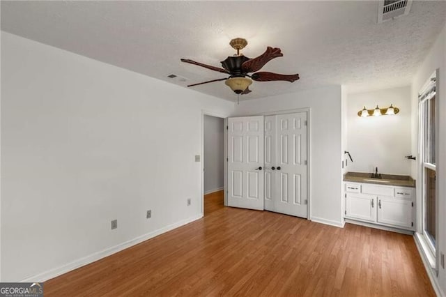 unfurnished bedroom featuring a sink, light wood finished floors, baseboards, a closet, and a textured ceiling