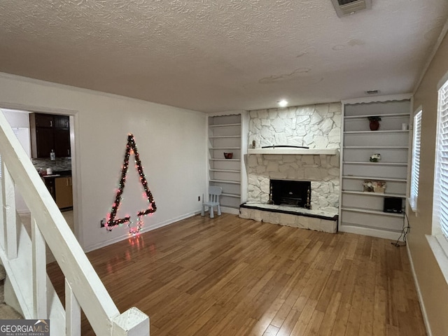 3709 Charlotte Dr, Rex, GA 30273 - unfurnished living room with a textured ceiling, hardwood / wood-style flooring, a stone fireplace, built in features, and baseboards