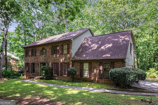 view of front of house featuring roof with shingles, brick siding, and a front lawn