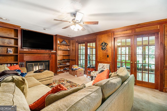 carpeted living room featuring french doors, healthy amount of natural light, a ceiling fan, wooden walls, and a glass covered fireplace