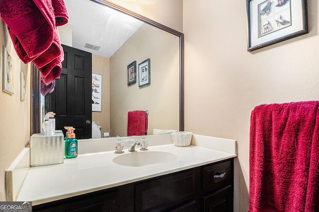 half bathroom featuring vanity, toilet, and a textured wall