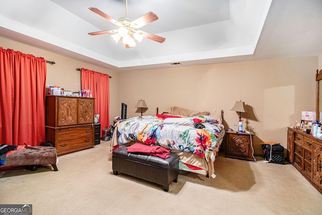 carpeted bedroom with a tray ceiling and a ceiling fan
