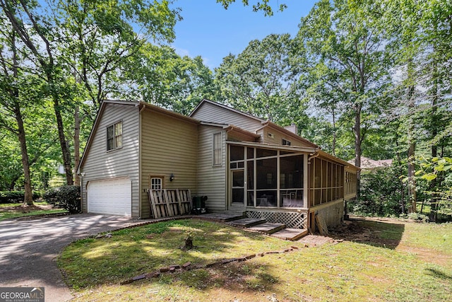 rear view of house with a sunroom, asphalt driveway, an attached garage, and a chimney