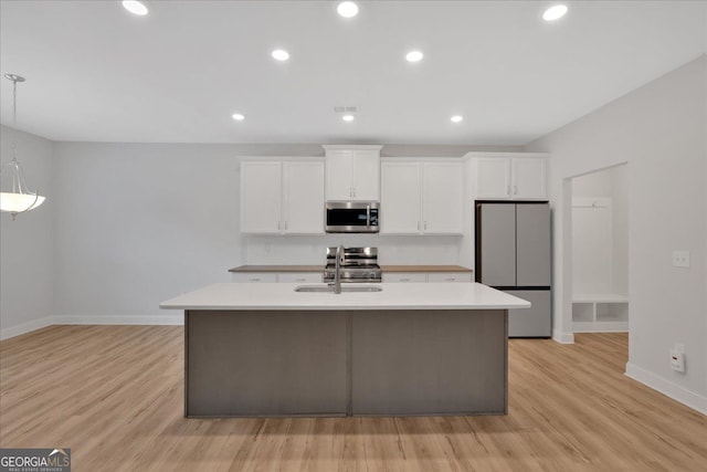 kitchen with appliances with stainless steel finishes, baseboards, a center island with sink, white cabinets, and light countertops