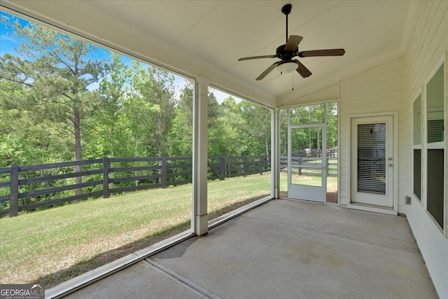 unfurnished sunroom with ceiling fan, vaulted ceiling, and view of wooded area
